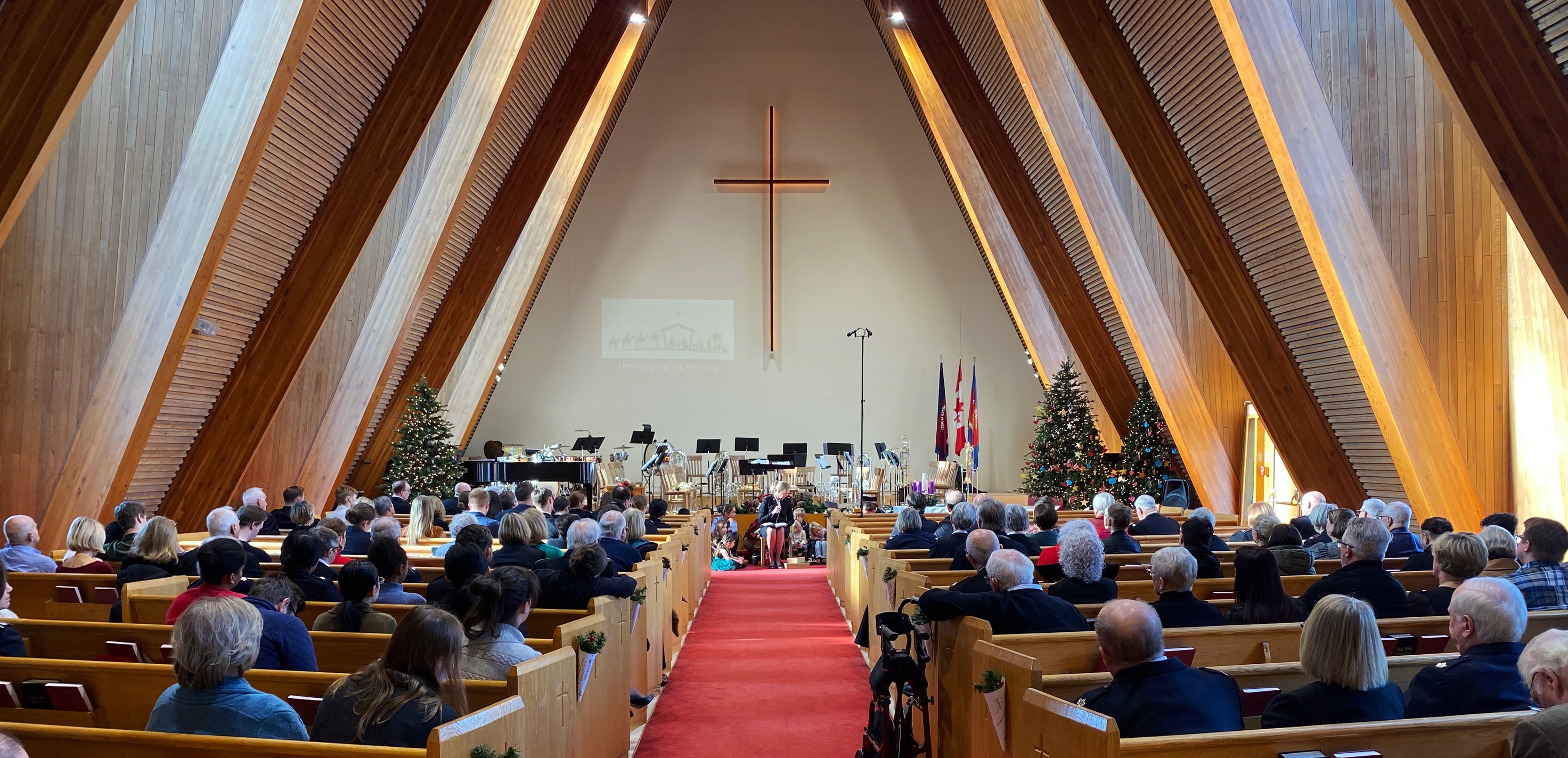 Congregation gathered inside Yorkminster Citadel’s sanctuary during a worship service, facing the platform with musicians, Christmas trees, and a large cross at the front.