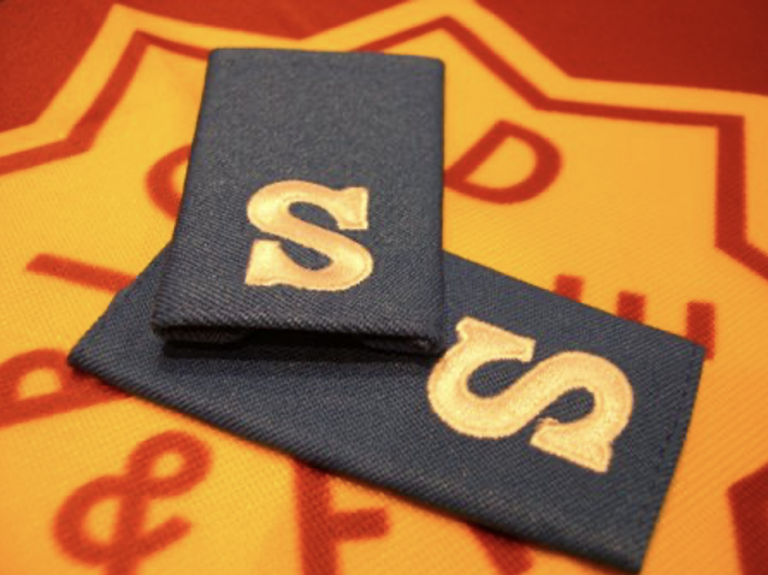 Close-up of Salvation Army Senior Soldier epaulettes with gold ‘S’ lettering.