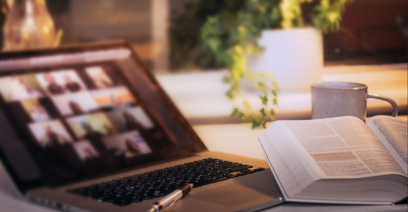 Open Bible and laptop on a desk displaying a Zoom meeting.