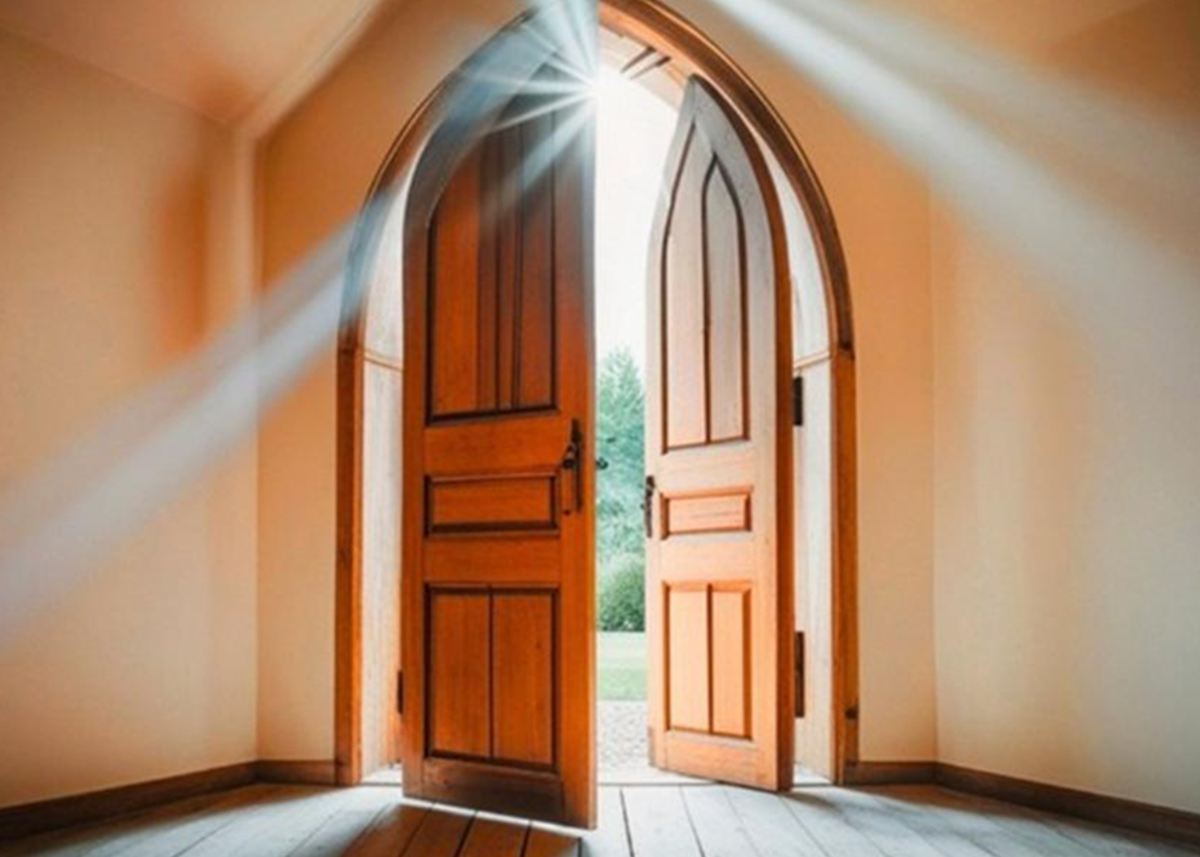 Sunlight streaming through open wooden church doors into a bright entryway.