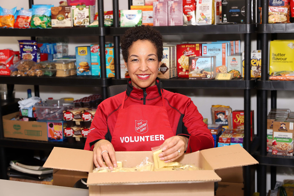 Volunteer in the Salvation Army apron packing food items into a box in a community food pantry.